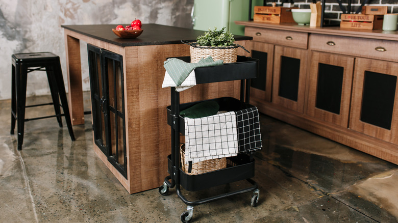 A rolling kitchen cart draped with kitchen towels, holding a plant and a basket