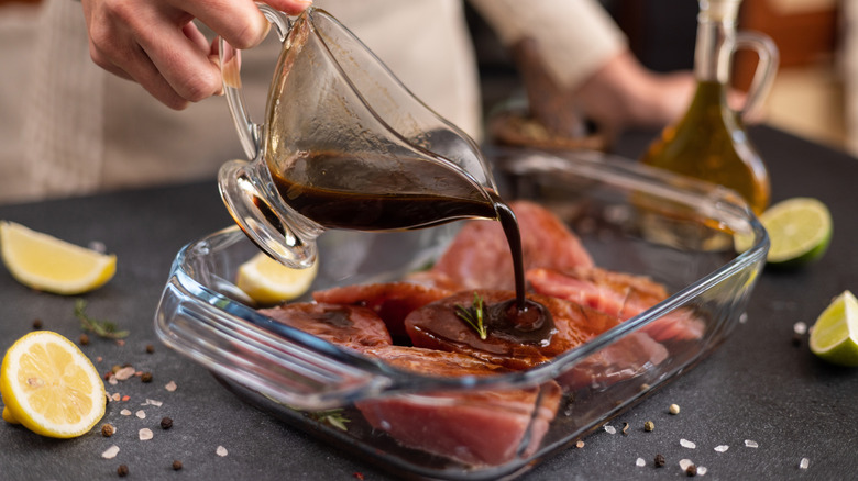 A chef pours marinade onto raw pieces of fish in glass dish