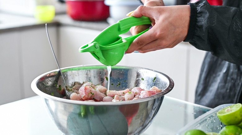 A person squeezes limes into a bowl of white fish.