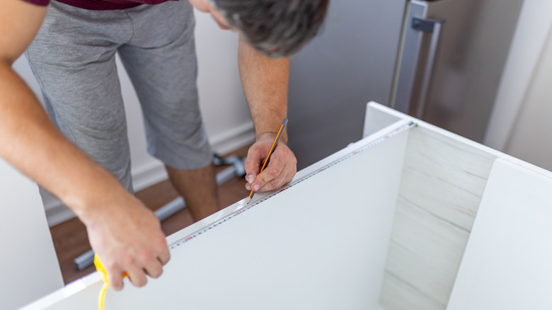 man measuring kitchen cabinet