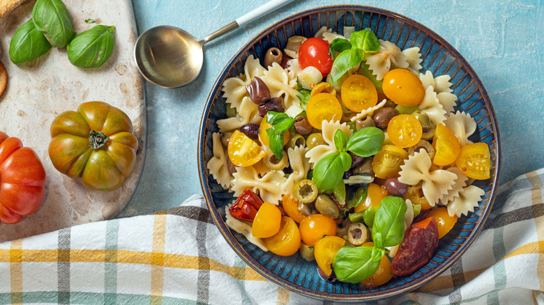 A bowl of farfalle pasta salad with tomatoes, olives, and fresh basil