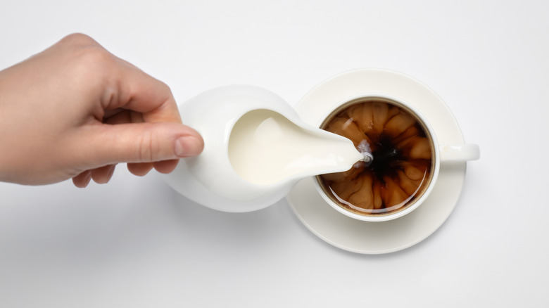 Hand pouring creamer into coffee