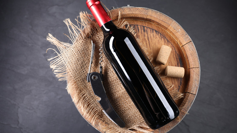 Sommelier corkscrew next to a bottle of wine and corks on a barrel