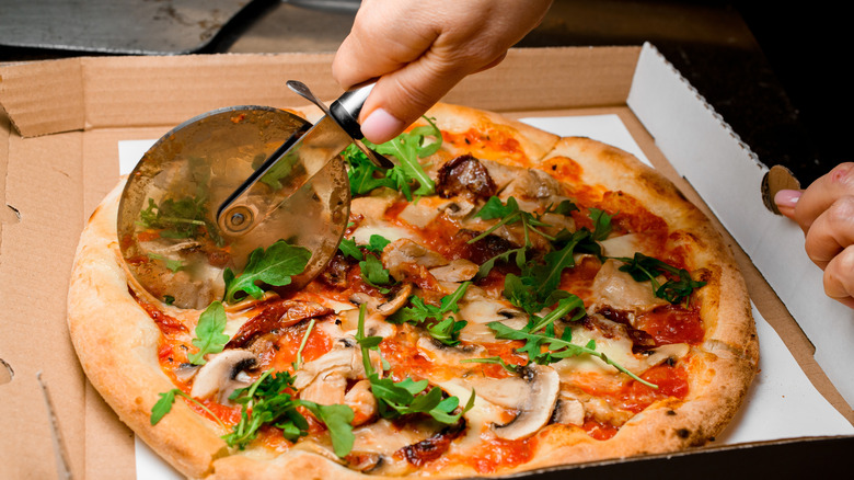 A person cutting a pizza using a pizza cutter.