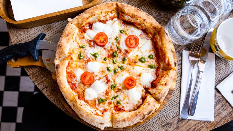 A finished pizza sits on a table next to utensils, water, and a pizza cutter.