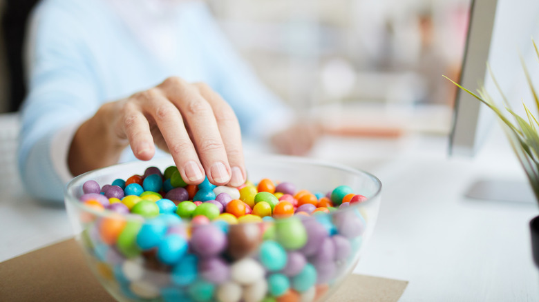 A woman reaches into a bowl of brightly colored round candies