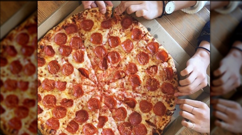 Hands shown taking slices from a Costco pepperoni pizza.