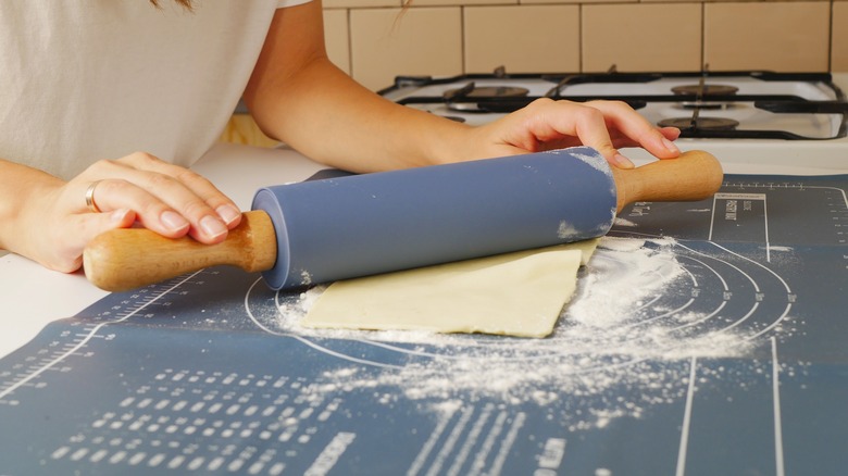 A cook rolls out puff pastry with a rolling pin on a floured surface