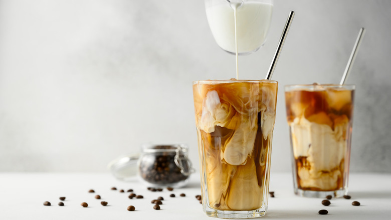 Milk pouring into a tall glass of iced coffee with straw