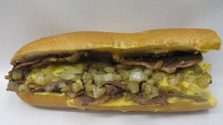 A Philly cheesesteak rests on a white background and is slathered in diced onions