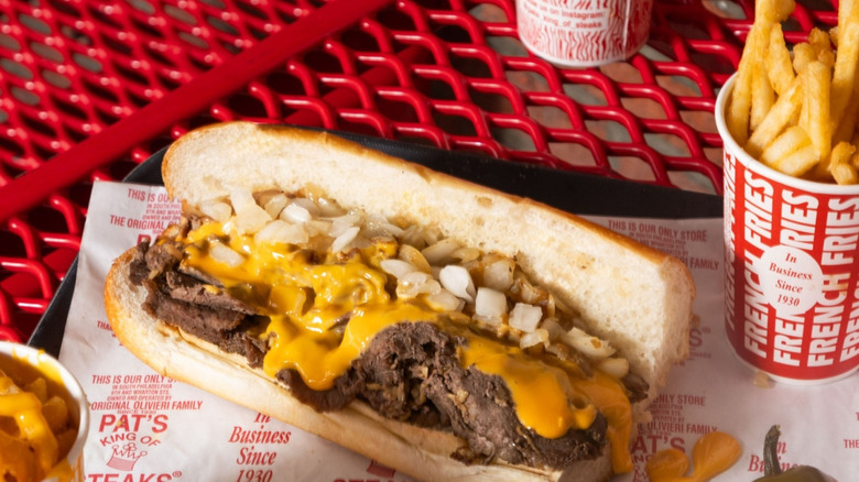 A Philly cheesesteak with a whole pickled pepper and a cup of fries from Pat's