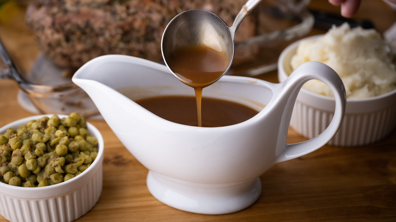 A white jug of gravy with bowls of peas and mashed potatoes