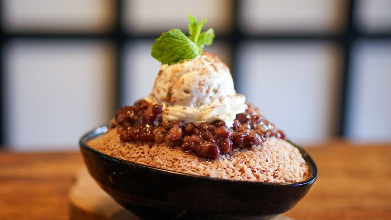 Bowl of red bean ice cream on a layer of red beans has a fresh sprig of mint on top