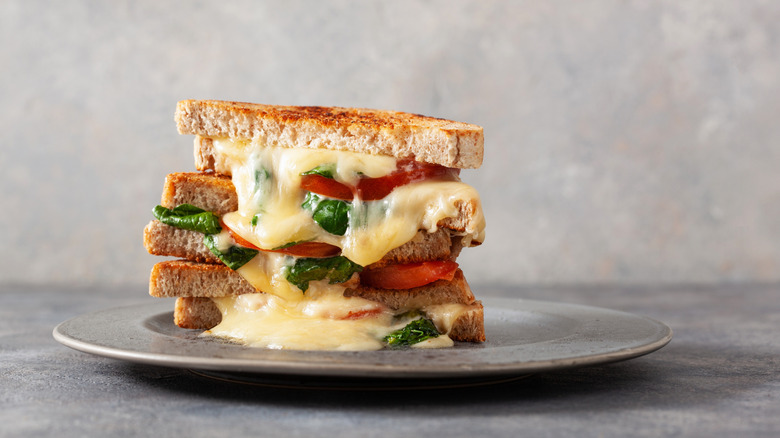 A melty grilled sandwich with tomato and spinach against a grey backgroud