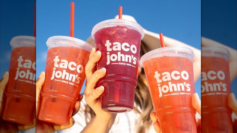 Three hands holding up drinks with the Taco John's logo