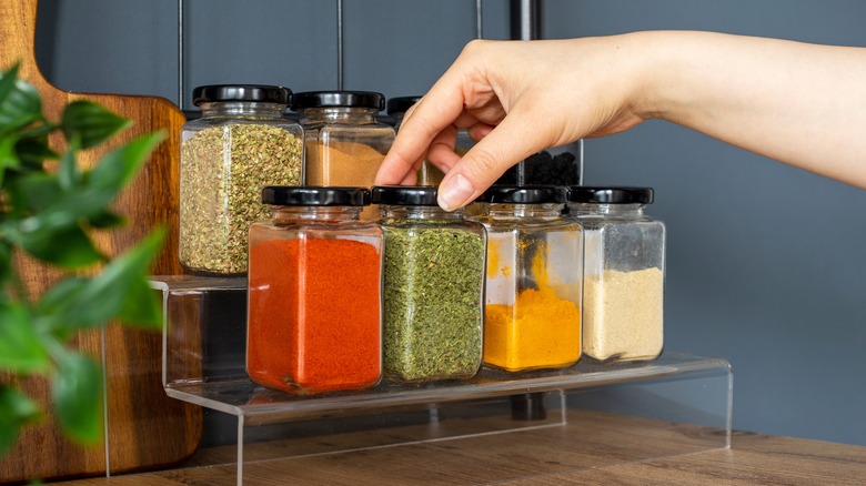 Person reaching for spice jars on rack