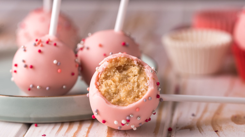 A pink frosted cake pop with a bite taken out of it sits on a wooden table