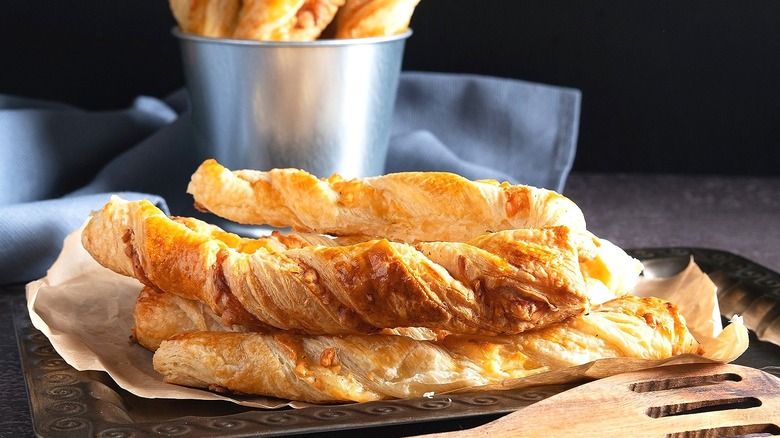 Puff pastry cheese twists on parchment paper over a metal serving tray