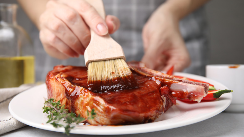 Chef basting a raw steak with marinade