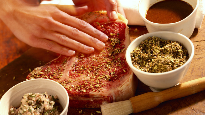 Chef rubbing dry seasonings onto a T-bone steak