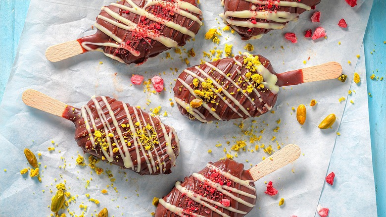 Pistachio ice cream popsicles covered in chocolate, crushed pistachios, and freeze-dried berries