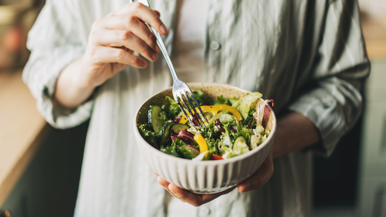 Person holding bowl of crunchy fresh salad with fork in hand