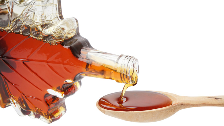 Maple syrup being poured from a maple leaf-shaped bottle onto a wooden spoon.