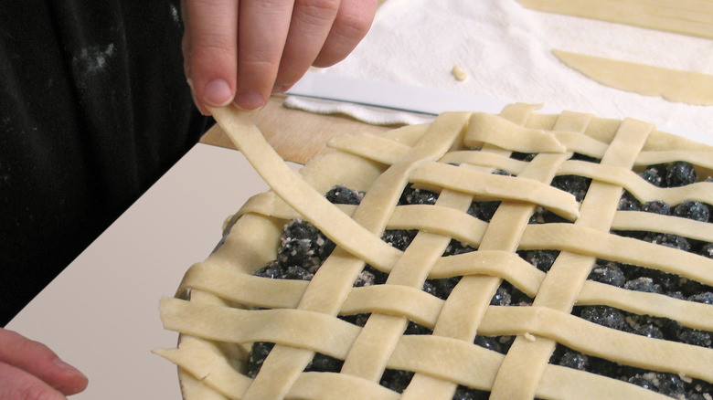 Person adding lattice top to blueberry pie