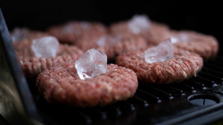 burger patties with ice cubes on top on the grill