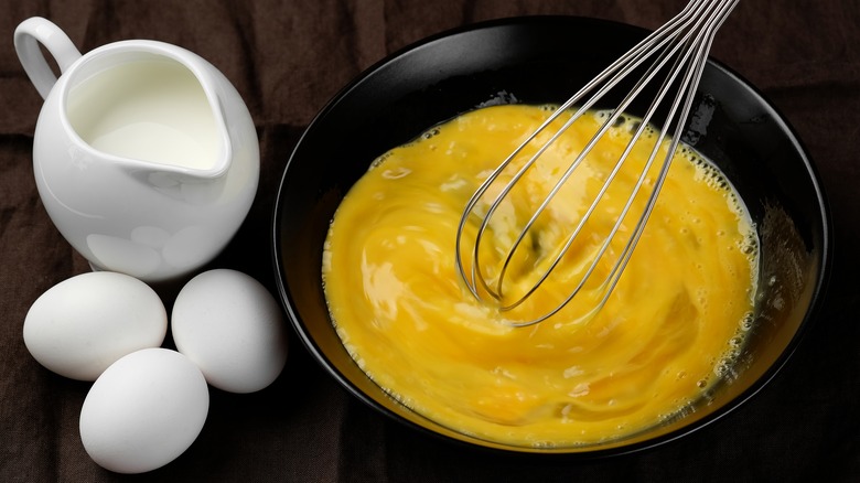 Scrambling eggs in pan with whisk and jug of cream
