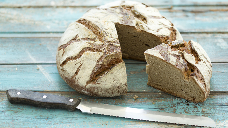 A bread knife and cut loaf of bread sit on blue table