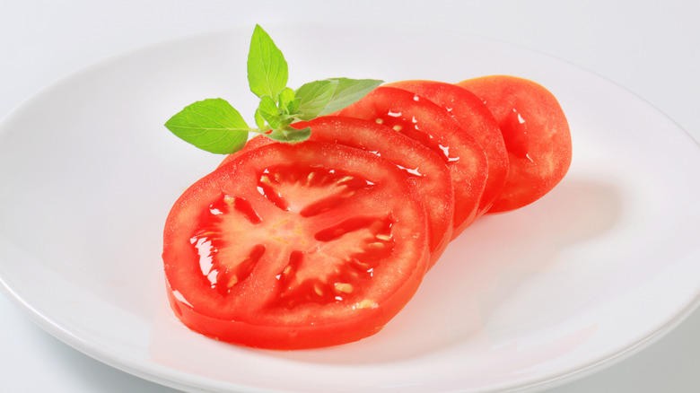 Sliced tomato rests on a plate with a basil garnish