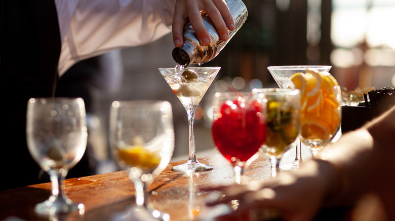 A bartender pouring a shaken martini into a glass with olives.