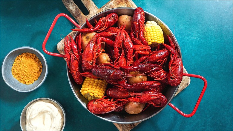 Crawfish boil in a pot with red handles and two small bowls of ground mustard and sour cream