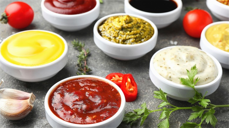 Various condiments like aioli and chili sauce in small white bowls