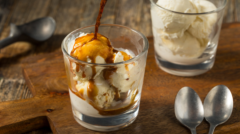 Two glasses of ice cream rest on a wooden board having espresso poured on top of them, creating affogato