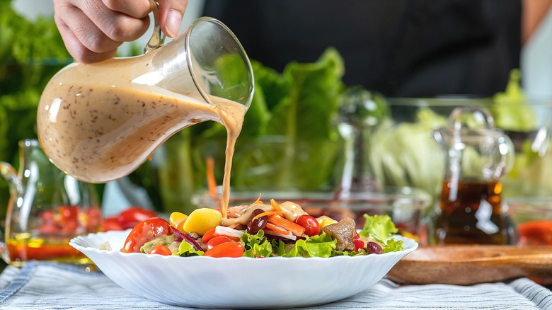 Hand pouring creamy dressing over plate of salad