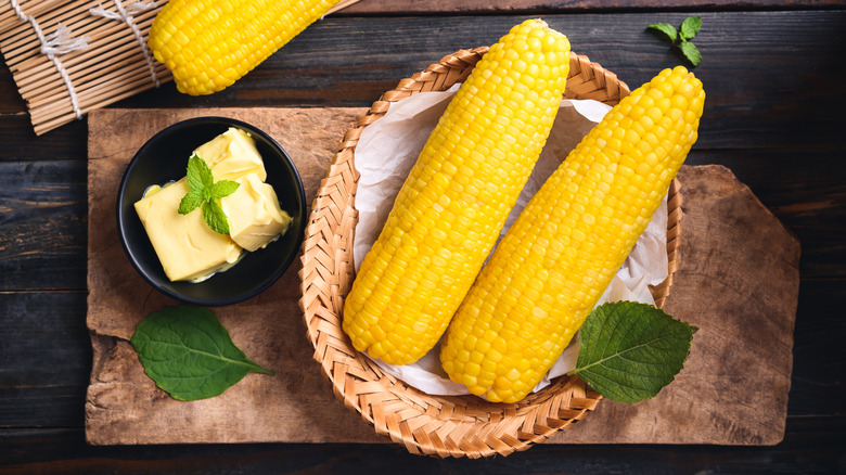 Two corn on the cob in a basket with butter
