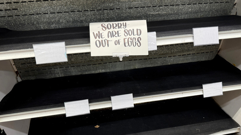 Empty grocery store shelves with sign reading, "sorry, we are all sold out of eggs"