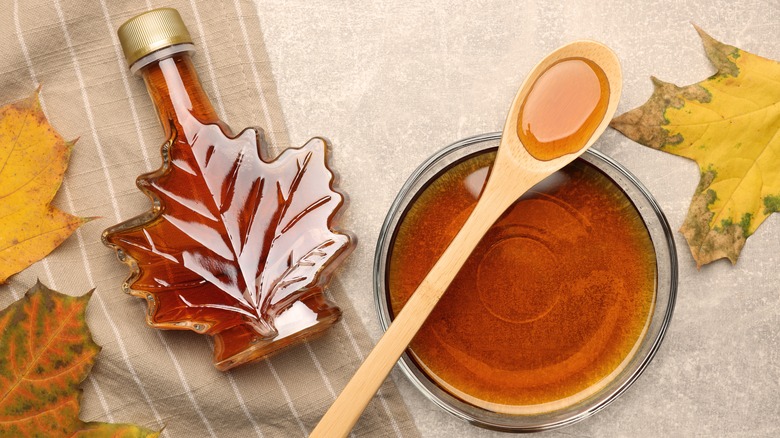 Maple syrup in leaf shaped bottle and poured into bowl with wood spoon