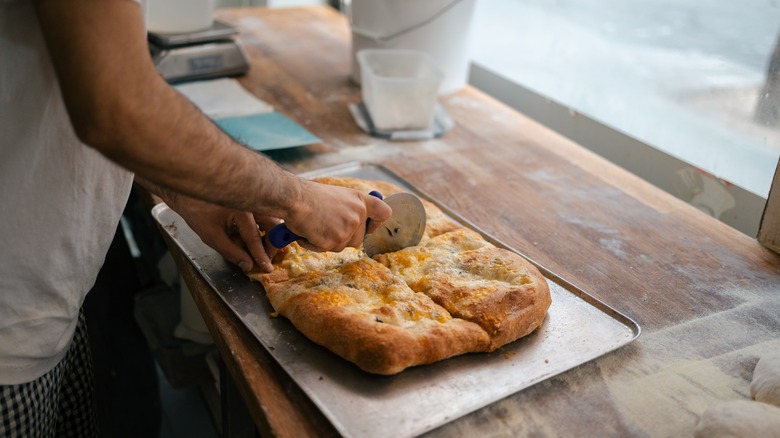 man cutting bread with pizza cutter