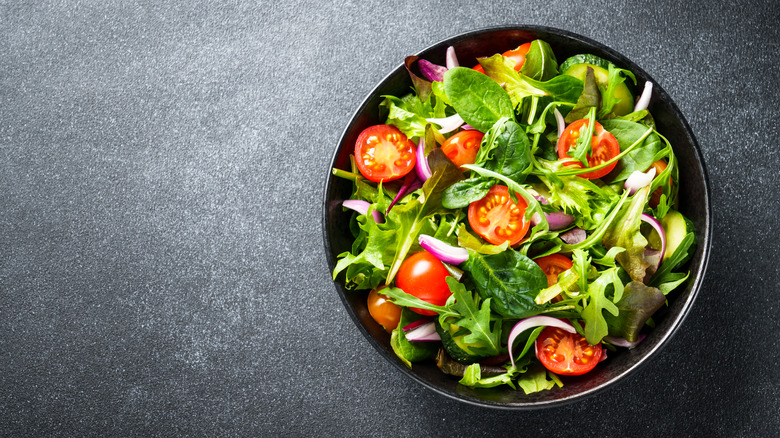 A bowl of salad with leafy greens, cherry tomatoes, cucumbers, and onions