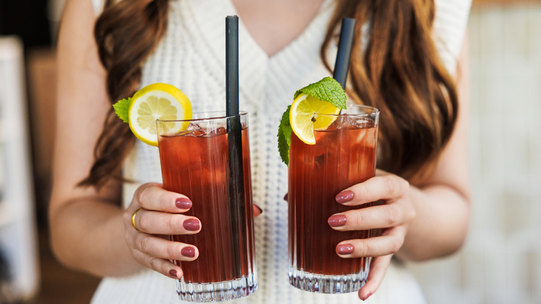 A woman holding two glasses of iced tea garnished with lemon and mint leaves.