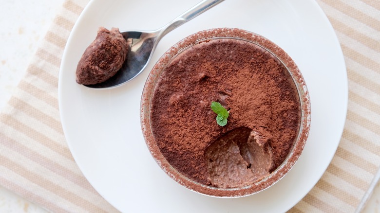 Chocolate mousse in glass cup topped with cocoa powder and sprig of mint