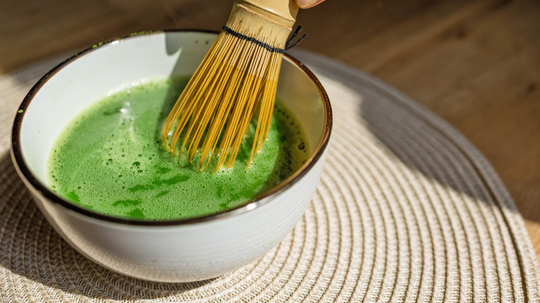 Matcha tea and hot water being whisked in a bowl with a bamboo whisk