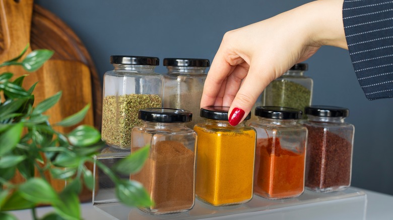 A hand selects a jar of spice from a spice rack.