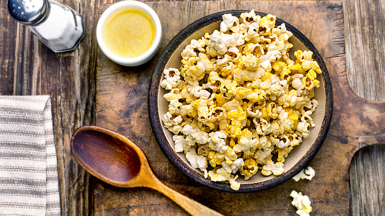 A bowl of popcorn with melted butter and salt on rustic wood table