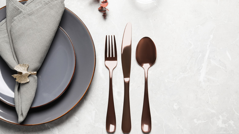 Close up of a table setting with a knife, fork, and spoon beside a set of gray plates and napkins