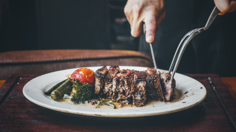 Close up of a person cutting their steak into pieces