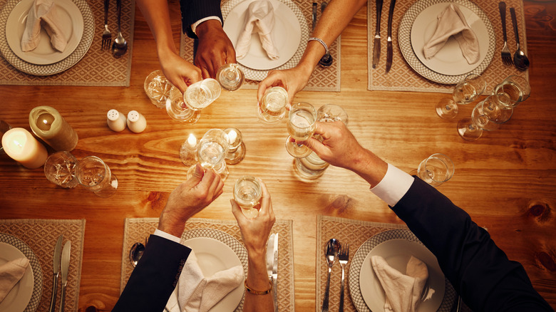 Many hands raise glasses in a toast across a formal dining table